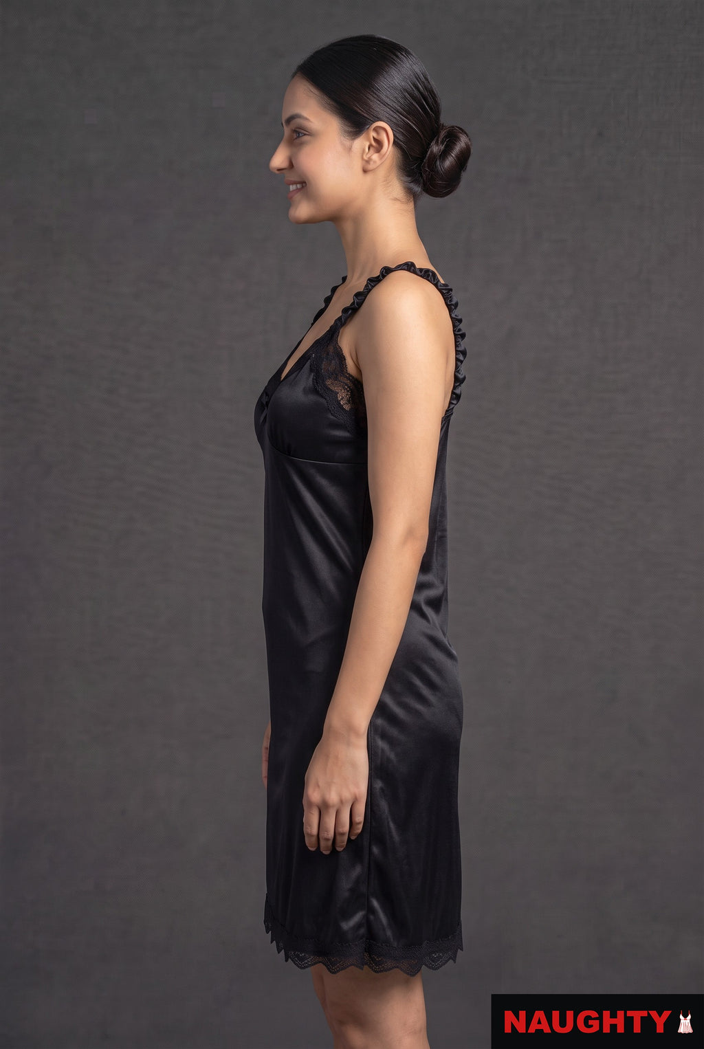 Naughty black silky satin nightdress with delicate lace trim and ruffled straps worn by a model in profile view