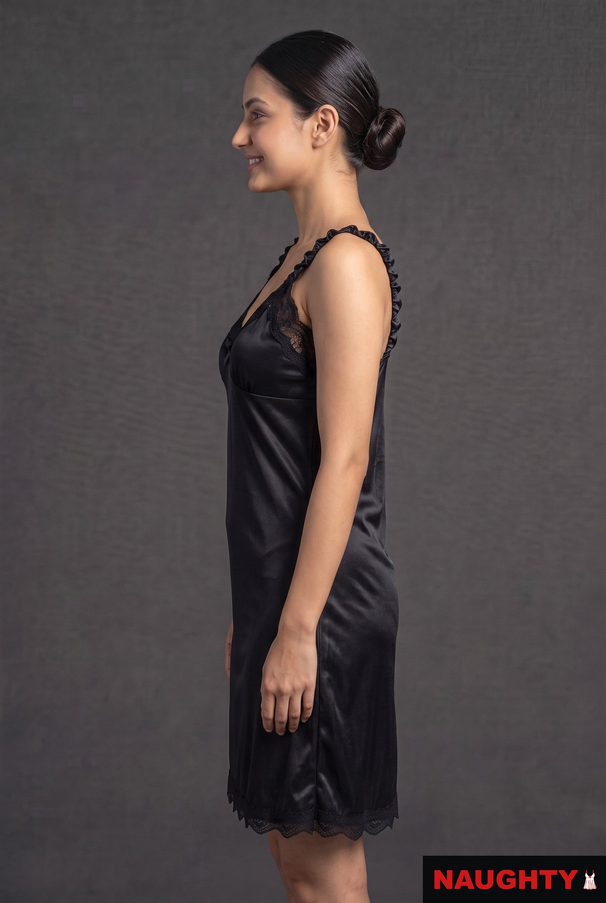 Naughty black silky satin nightdress with delicate lace trim and ruffled straps worn by a model in profile view