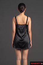 Back view of a woman wearing a Naughty black silky satin nightdress with gathered straps against a grey background